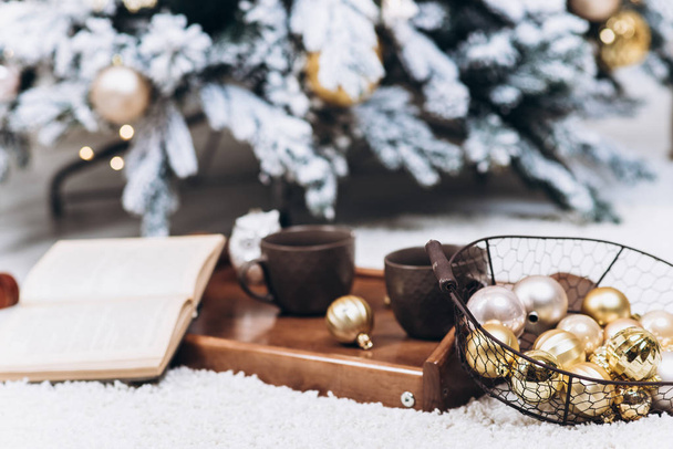 Una bandeja con dos tazas de bebidas calientes y un libro, un árbol de Navidad en el fondo. Concepto de Navidad y Año Nuevo
 - Foto, Imagen