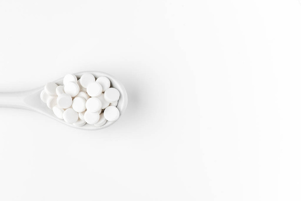 Pilules sur la cuillère et dispersées sur la surface blanche
 - Photo, image