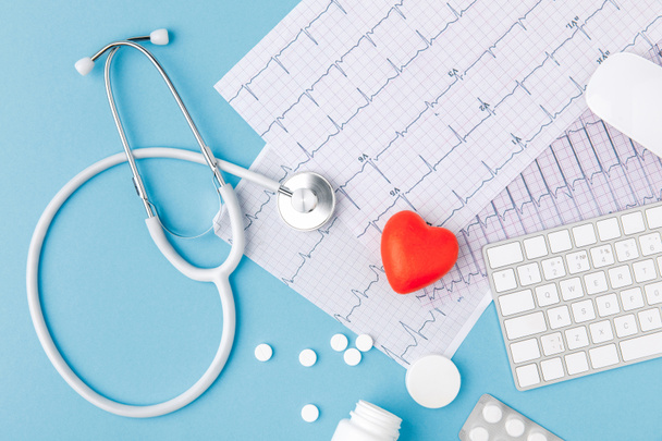 stetoscopio, carta con cardiogramma, pillole sparse, cuore rosso e tastiera isolati su sfondo blu
   - Foto, immagini