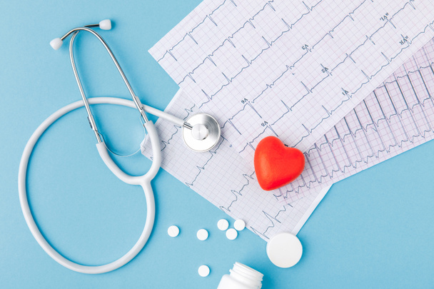 stetoscopio, carta con cardiogramma, pillole sparse e cuore rosso isolato su sfondo blu
   - Foto, immagini