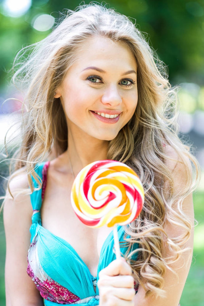 Aantrekkelijke blonde meisje met een lolly in het park in de zomer - Foto, afbeelding