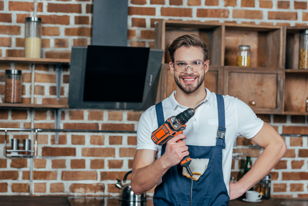 handsome young man holding electric drill and smiling at camera - Photo, Image