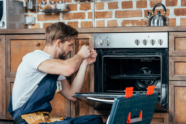 молодий ремонтник в захисному робочому одязі, що фіксує піч на кухні
 - Фото, зображення