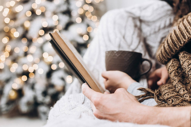 Un livre et une tasse de boisson chaude dans les mains d'un arbre de Noël. Noel et Nouvel An concept
 - Photo, image