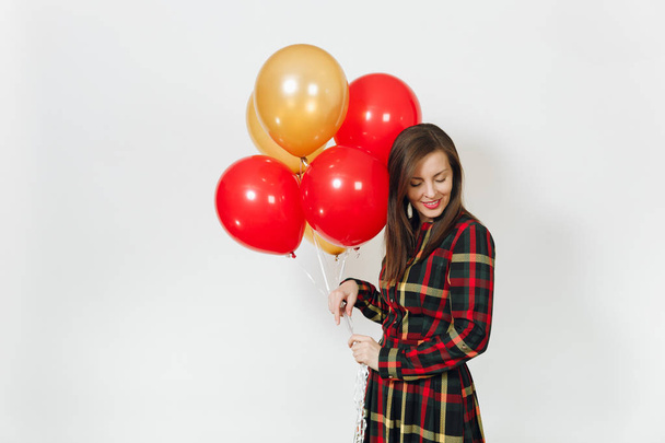 Beautiful caucasian young happy woman in long plaid checkered dress with shy charming smile, red, yellow golden balloons, celebrating birthday, on white background isolated. Holiday, party concept. - Фото, изображение