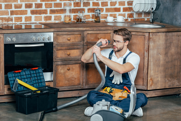 young repairman in protective glasses checking broken vacuum cleaner  - Fotoğraf, Görsel
