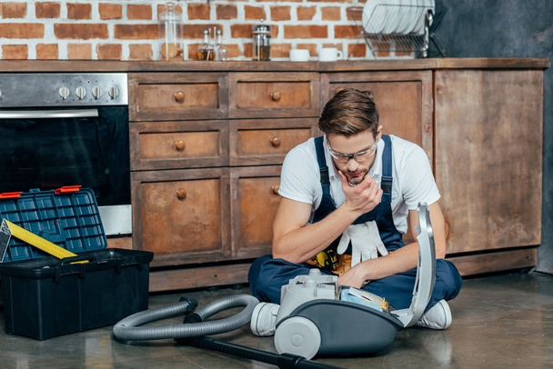 young repairman in protective glasses looking at broken vacuum cleaner  - Foto, Imagem