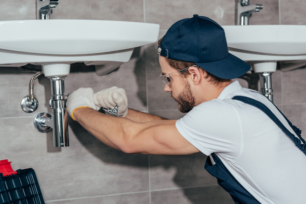 крупным планом молодой профессиональный сантехник чинит раковину в ванной комнате
 - Фото, изображение