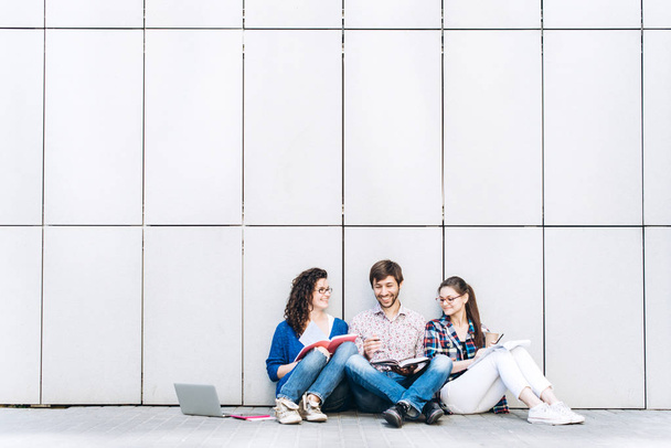 Persone con libri e gadget seduti sul pavimento vicino al muro. Educazione concetto di social media
. - Foto, immagini