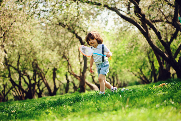 幸せな 3 歳子少年は日当たりの良い庭や公園で散歩に網で蝶をキャッチします。春と夏の野外活動、幸せな子供時代のコンセプト. - 写真・画像