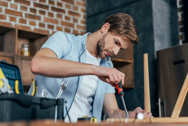 focused young man repairing stool with screwdriver - Photo, Image