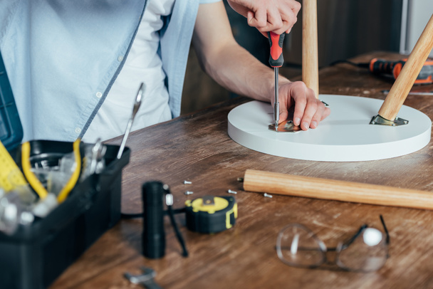 cropped shot of man repairing stool with screwdriver  - Foto, afbeelding