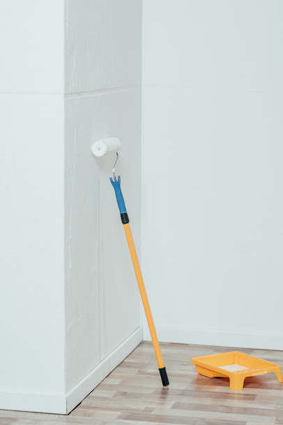 painting roller and container with white paint in empty room - Photo, Image
