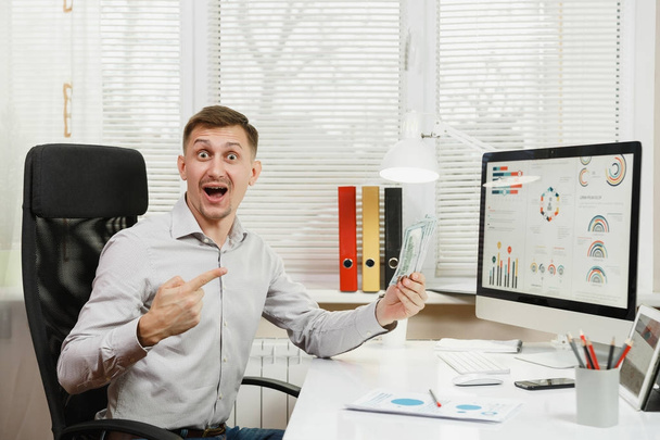 Handsome smiling business man in shirt sitting at the desk with  - Photo, Image