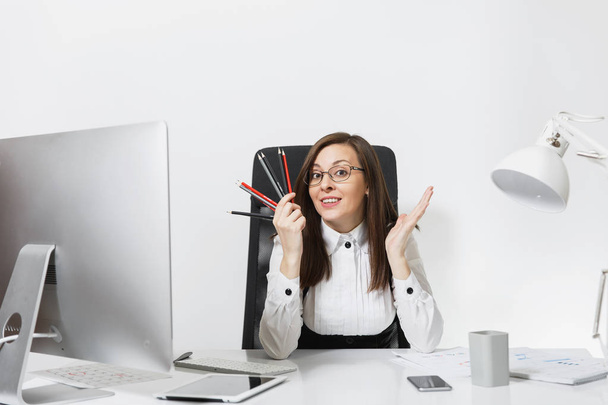 Krásná usměvavá hnědé vlasy obchodní žena v obleku sedí u stolu s tužky, práce na počítači s moderní monitor s dokumenty v kanceláři světlo, při pohledu na fotoaparát na bílém pozadí - Fotografie, Obrázek