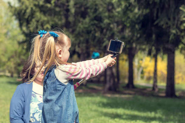 Cute little blonde girl with two ponytails taking selfie in the  - Zdjęcie, obraz