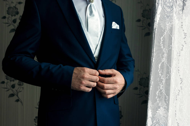 Un hombre con un traje azul endereza sus mangas
 - Foto, imagen