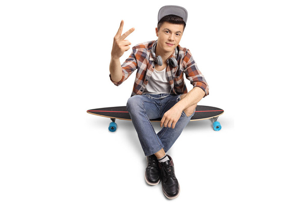 hipster sitting on a longboard and making a peace sign - Фото, изображение