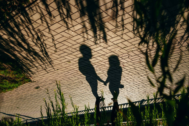 Shadows of a loving couple holding hands in the city center on cobblestones on a sunny day. - Foto, imagen