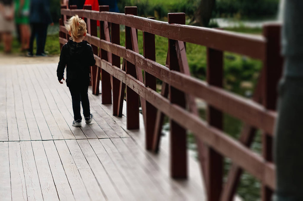 little girl on a wooden bridge with her back to the camera in the park at sunset - Фото, изображение