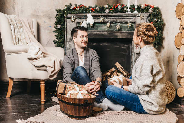 Beautiful couple sitting at the fireplace with gift boxes. Christmas and New Year concept - Foto, afbeelding