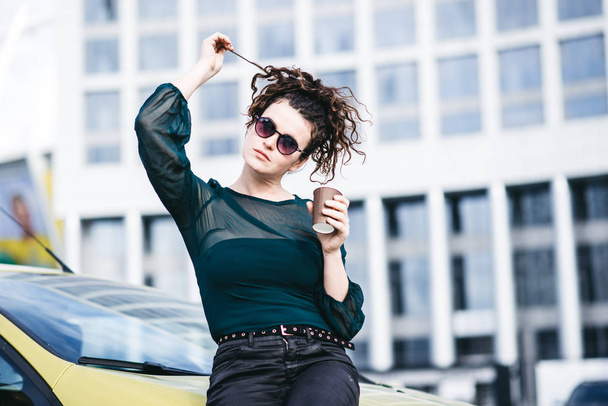 Modieuze meisje permanent in de buurt van haar auto in de moderne stad - Foto, afbeelding