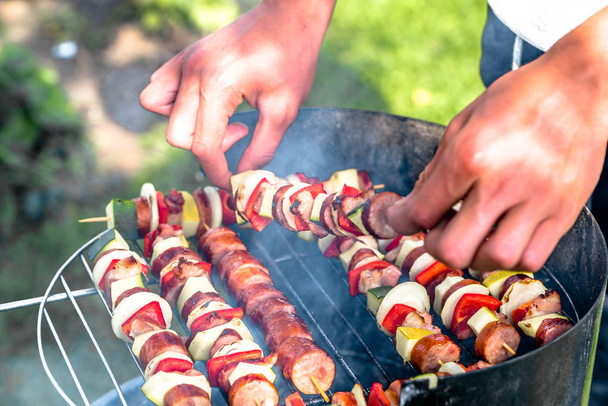 Grillu szaszłyki na grilla w ogrodzie, ręce kucharza przygotowuje shashliks z warzyw i mięsa, odkryty grill na trawie - Zdjęcie, obraz