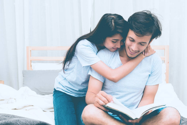 Mixed race lovers concept. Young white male reading a book in his bedroom with his pretty young chinese girlfriend to join. Wearing blue jeans, blue shirt and in their early twenties. Taken indoor. - Photo, image