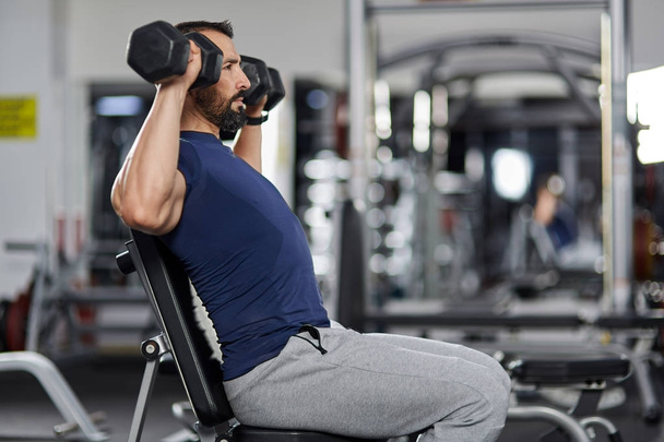 Man doing shoulder workout with dumbbells in the gym - 写真・画像