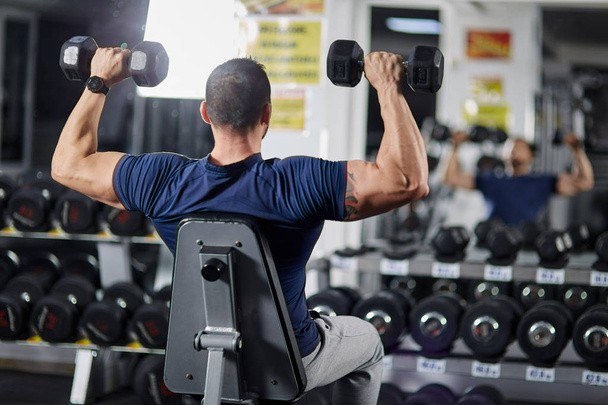 Man doing shoulder workout with dumbbells in the gym - Foto, afbeelding