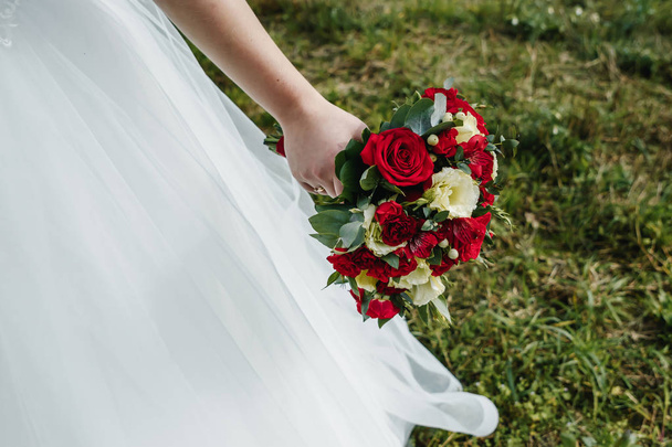 Close up of a bride holding a wedding bouquet with red and white roses. - 写真・画像