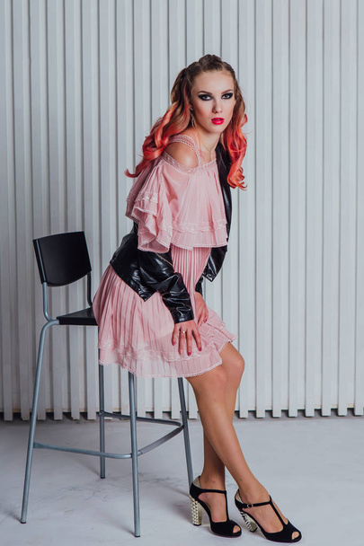 Beautiful young woman with bright make up and pink hair in leather jacket and pink dress posing in studio. - 写真・画像