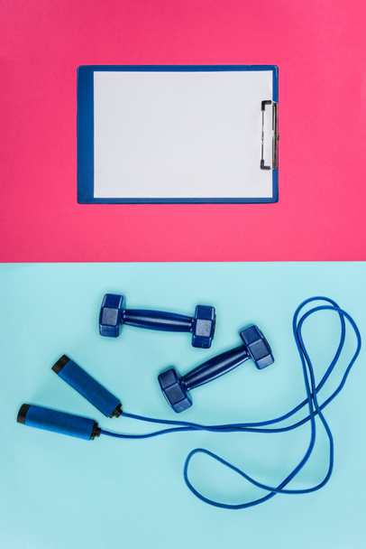 Sport súlyzó, csipeszes írótábla és ugró kötél elszigetelt rózsaszín és kék - Fotó, kép