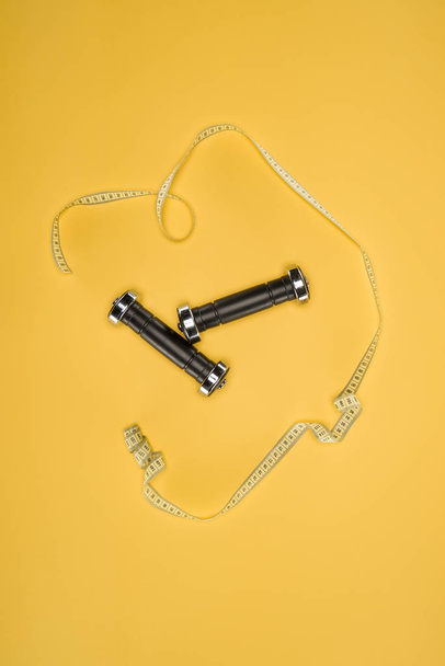 Sports dumbbells and measuring tape isolated on yellow - Fotografie, Obrázek