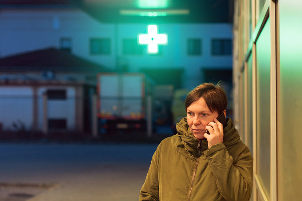 Mujer preocupada hablando por teléfono móvil frente a la farmacia
 - Foto, imagen