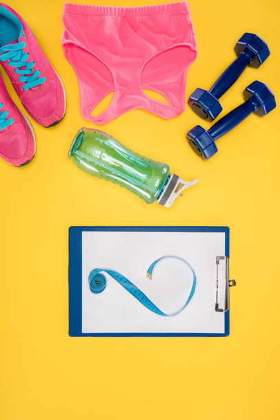 Sports equipment with shoes, dumbbells, sports top and clipboard isolated on yellow - Fotó, kép
