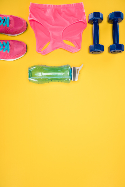Urheiluvälineet kengät, käsipainot, urheilutoppi ja vesipullo eristetty keltaisella
 - Valokuva, kuva