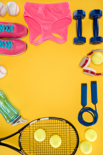 Sports equipment with shoes, dumbbells, sports top and headphones isolated on yellow - Photo, image