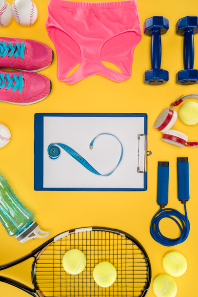 Equipamiento deportivo con zapatos, mancuernas, top deportivo y portapapeles aislados en amarillo
 - Foto, imagen