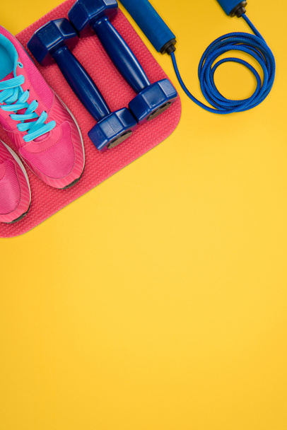 Sports equipment with shoes, dumbbells and skipping rope isolated on yellow - Photo, Image