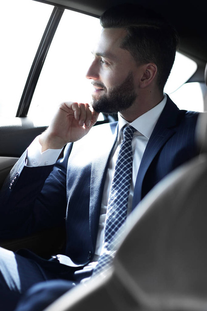 Smiling business man sitting in the back seat of a car - Foto, afbeelding
