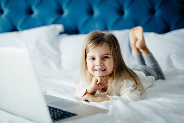 Little beautiful girl with a laptop on bed. - Φωτογραφία, εικόνα