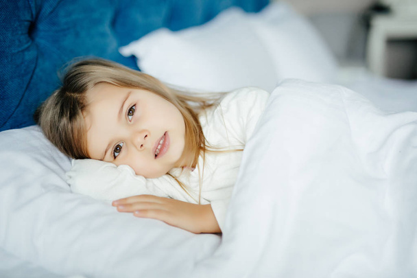 Close-up πορτρέτο του όμορφη μικρό παιδί ξαπλωμένος στο κρεβάτι με το χέρι κάτω από το μαξιλάρι, βλέπουν κάμερα στο σπίτι - Φωτογραφία, εικόνα