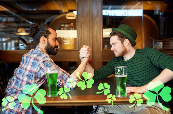 men drinking green beer and arm wrestling at pub - 写真・画像