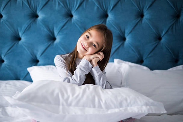 Маленькая девочка в спальне сидит на кровати. Маленькая девочка в пижаме и сидит в постели, держа подушку
 - Фото, изображение