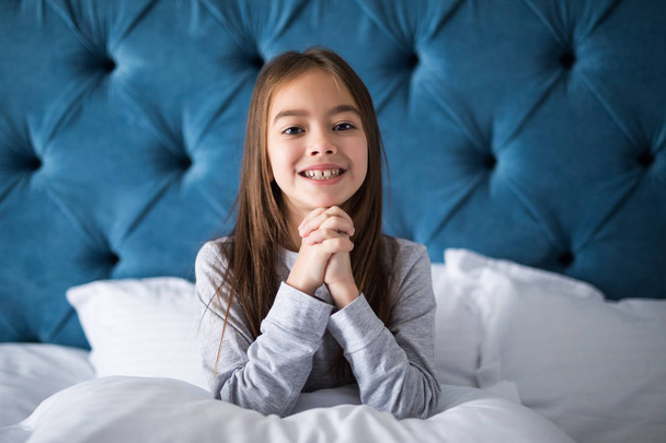linda niña sonriente despertó en la cama blanca sosteniendo la almohada
 - Foto, imagen