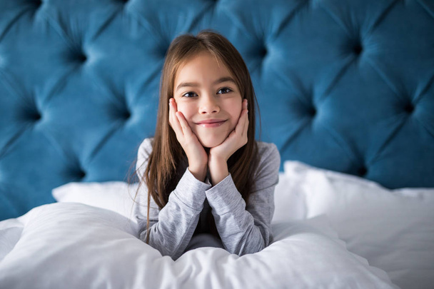 счастливая маленькая девочка с улыбкой и подушкой в постели дома
 - Фото, изображение