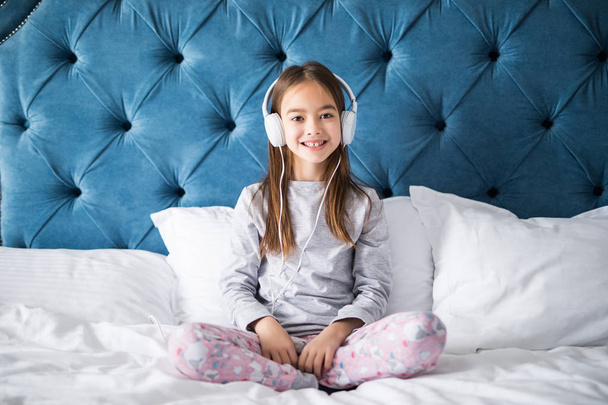 Niña feliz escuchando música con sonrisa mientras está sentada en su cama
 - Foto, imagen