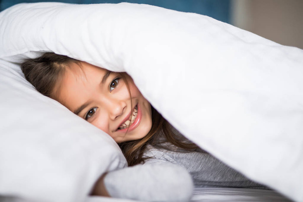 girl lying under a blanket in the bed and smiling at home - Foto, imagen