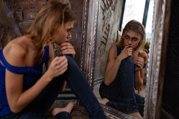 Donna vittima di violenza domestica e abusi siede sul pavimento vicino allo specchio e vede lividi e ferite sul viso e sulle mani
. - Foto, immagini